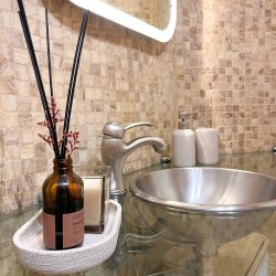 Detalle del baño del departamento Nicasio en La Latina, Madrid, con lavabo de acero inoxidable, encimera de cristal, difusor aromático y vela decorativa, gestionado por Stag Properties y destinado a alquiler vacacional