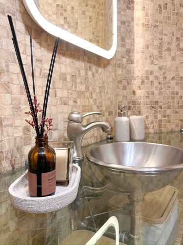 Detalle del baño del departamento Nicasio en La Latina, Madrid, con lavabo de acero inoxidable, encimera de cristal, difusor aromático y vela decorativa, gestionado por Stag Properties y destinado a alquiler vacacional